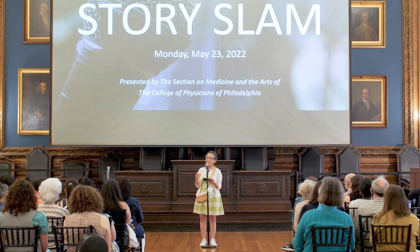 Woman standing at microphone in front of a large screen that says "STORY SLAM"